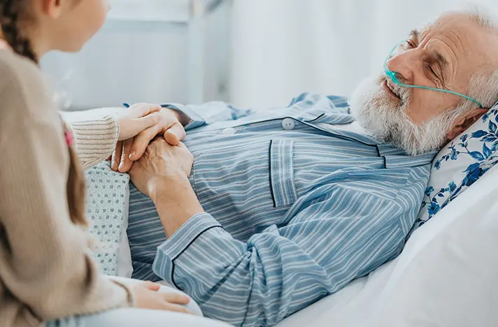 Caregiver gently holding the hand of an older man during hospice and comfort care at home