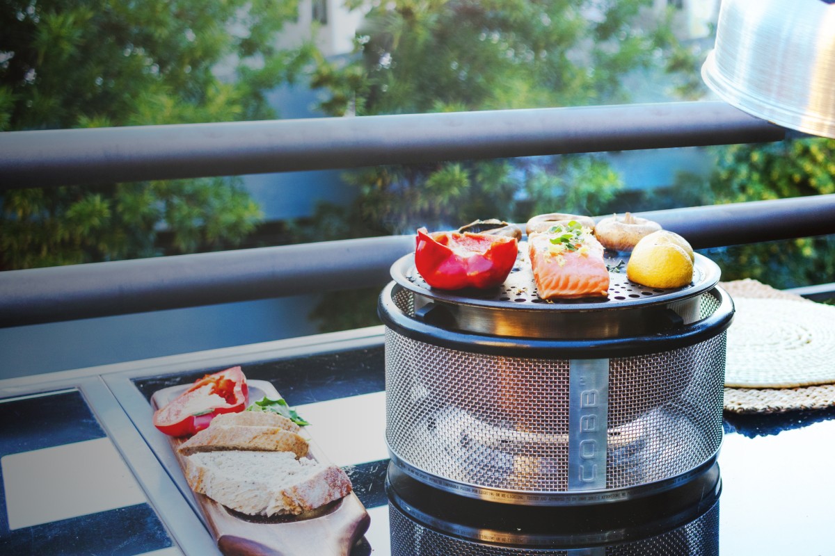 Parrilla COBB Premier en un balcon asando salmón y verduras