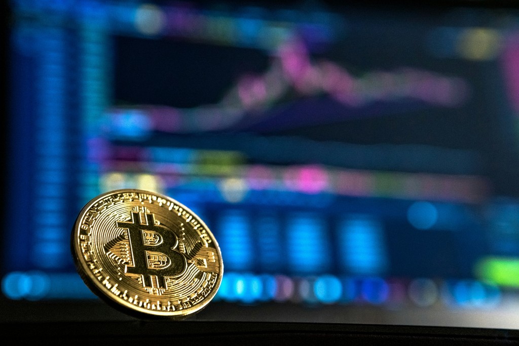 gold bitcoin coin in front of a monitor