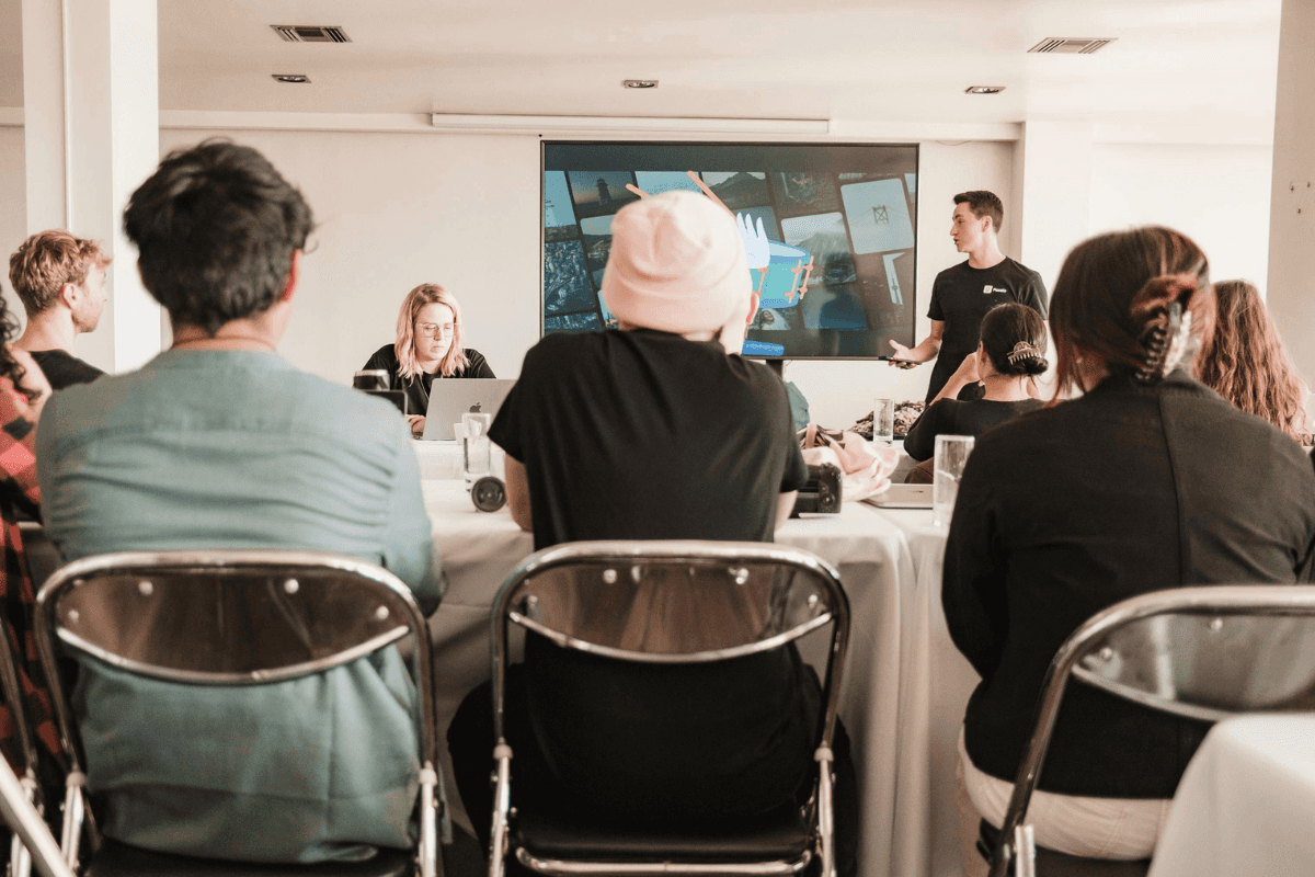People gathered in a room with tables and chairs, one person sitting.