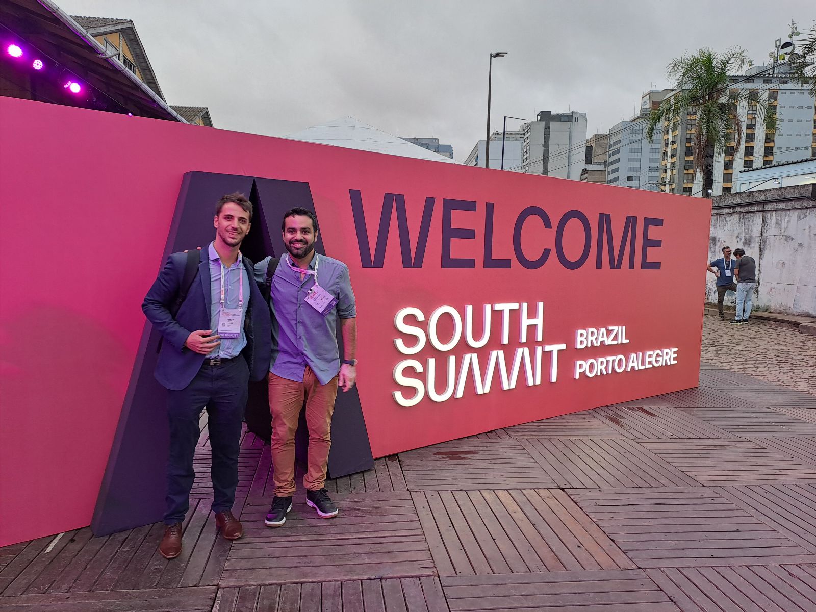 Founders smiling stand in front of the event sign reading "WELCOME SOUTH SUMMIT BRAZIL PORTO ALEGRE." 