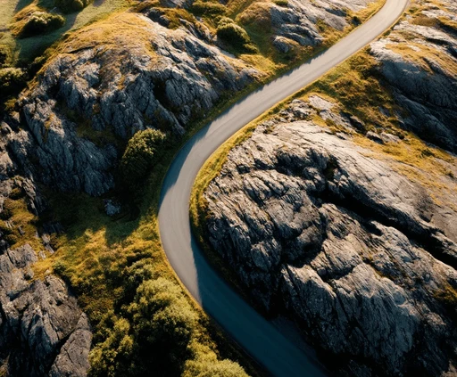 A winding road cuts through rocky terrain, surrounded by patches of green grass and illuminated by sunlight.