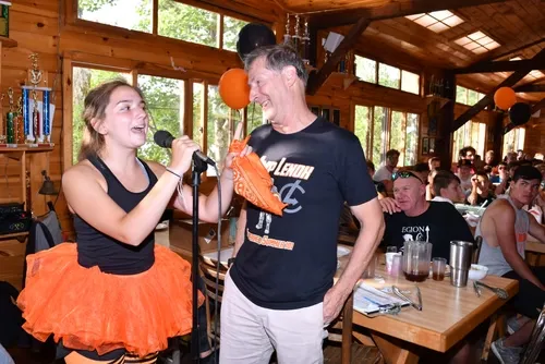 Camper singing into a microphone beside Rich Moss in the dining hall
