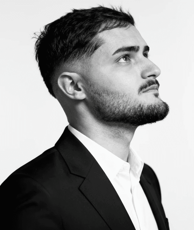 Portrait of a young man with short hair, wearing a dark t-shirt, against a plain background.