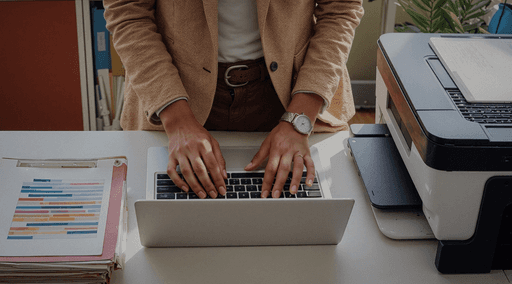 A person is standing at a desk while typing on a laptop.