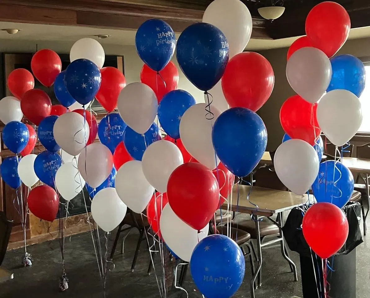 A vibrant arrangement of red, white, and blue balloons fills a room, tied to chairs and tables, creating a festive birthday party atmosphere.