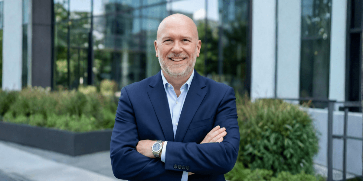 A bald man in a suit and tie stands confidently in front of a building, representing leadership in retirement planning.