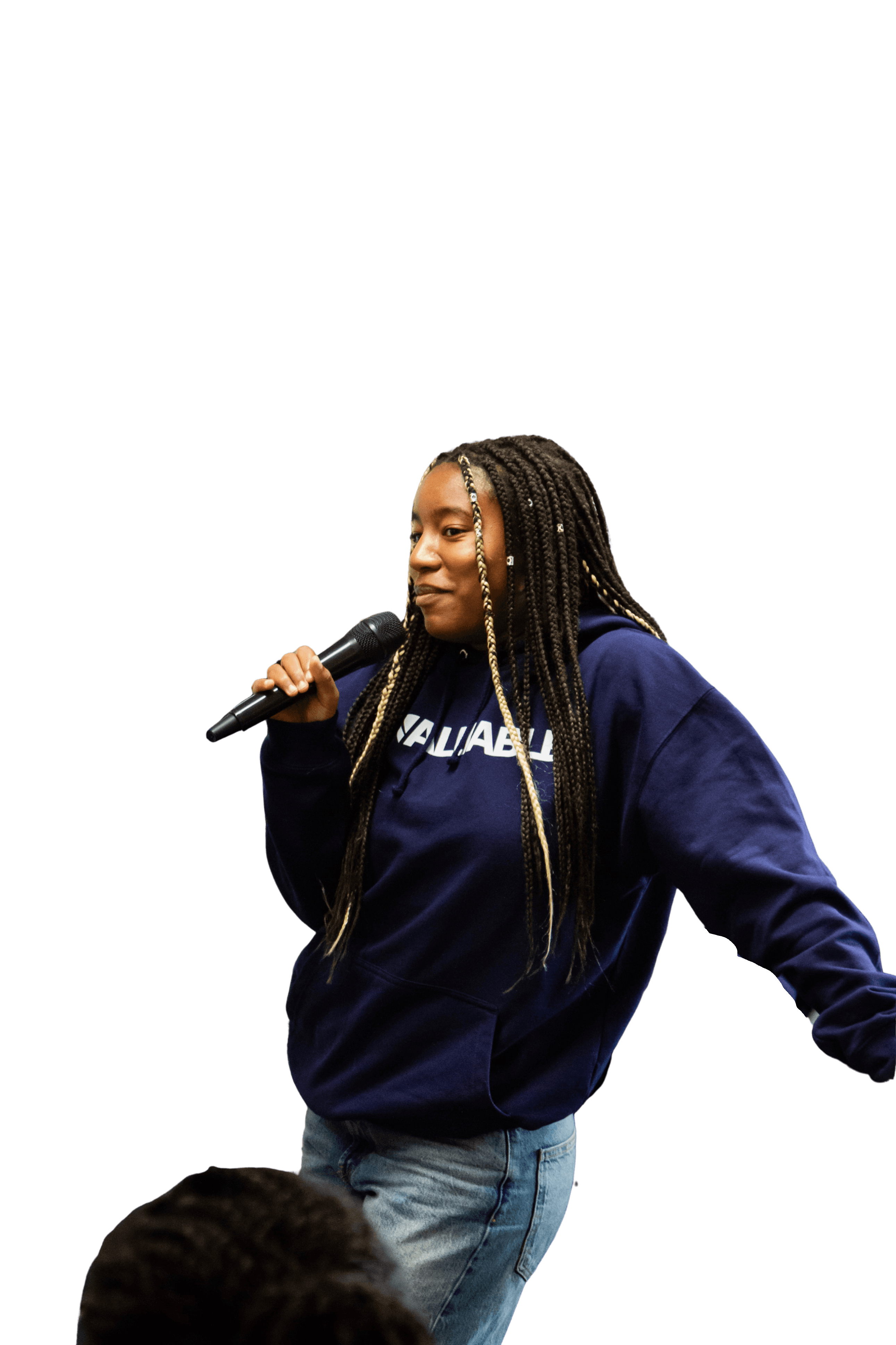 Young woman with braided hair wearing a navy valuable hoodie and jeans, holding a microphone and speaking.