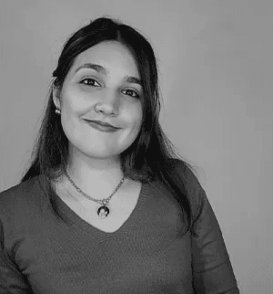 Casual studio portrait of a bearded man with curly hair in a white shirt, arms crossed, on a light gray background.