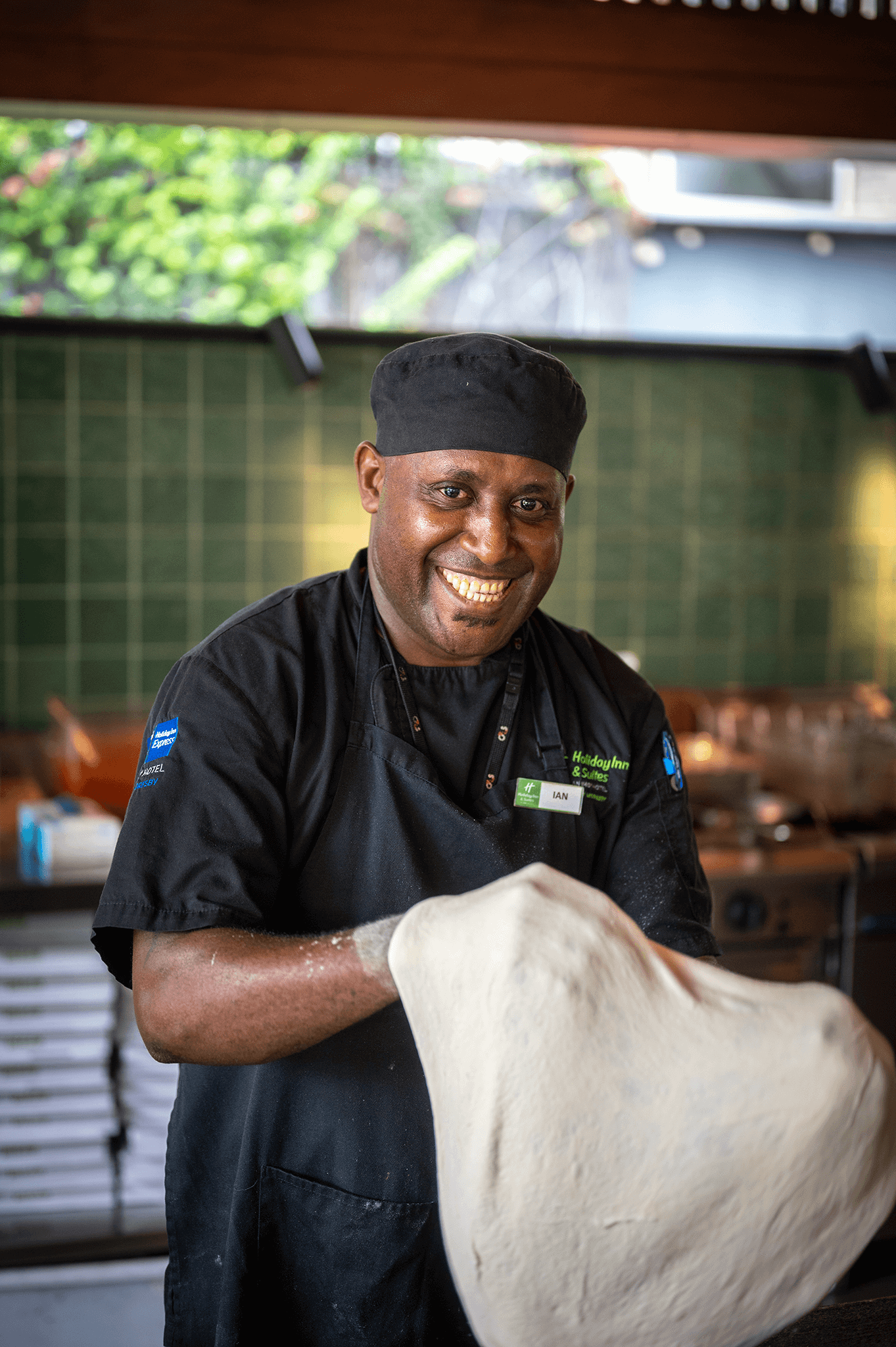 Smiling FAYA HAUS chef tossing pizza dough with expertise in an open kitchen setting.