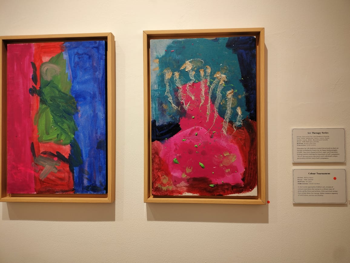 Two exhibits in a gallery, alongside their descriptions, painted in red, green, and blues.