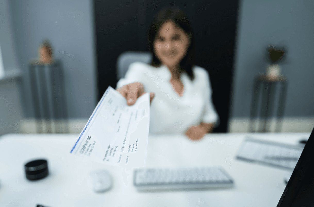 A blurred close-up view of a person's hand holding a check or document from "COMPANY INC." against a dark background.