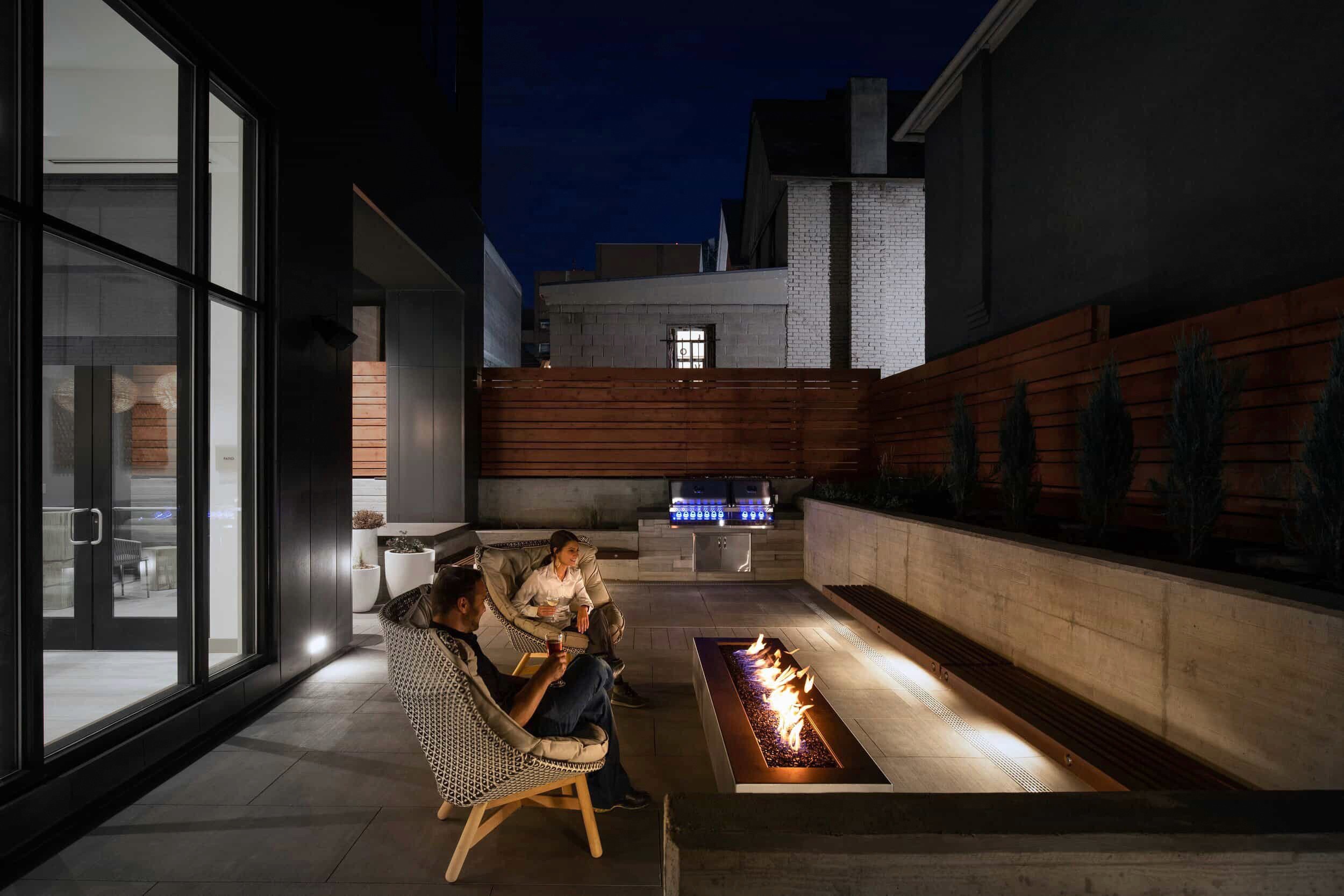 Couple relaxes by fire pit on a modern patio at night.