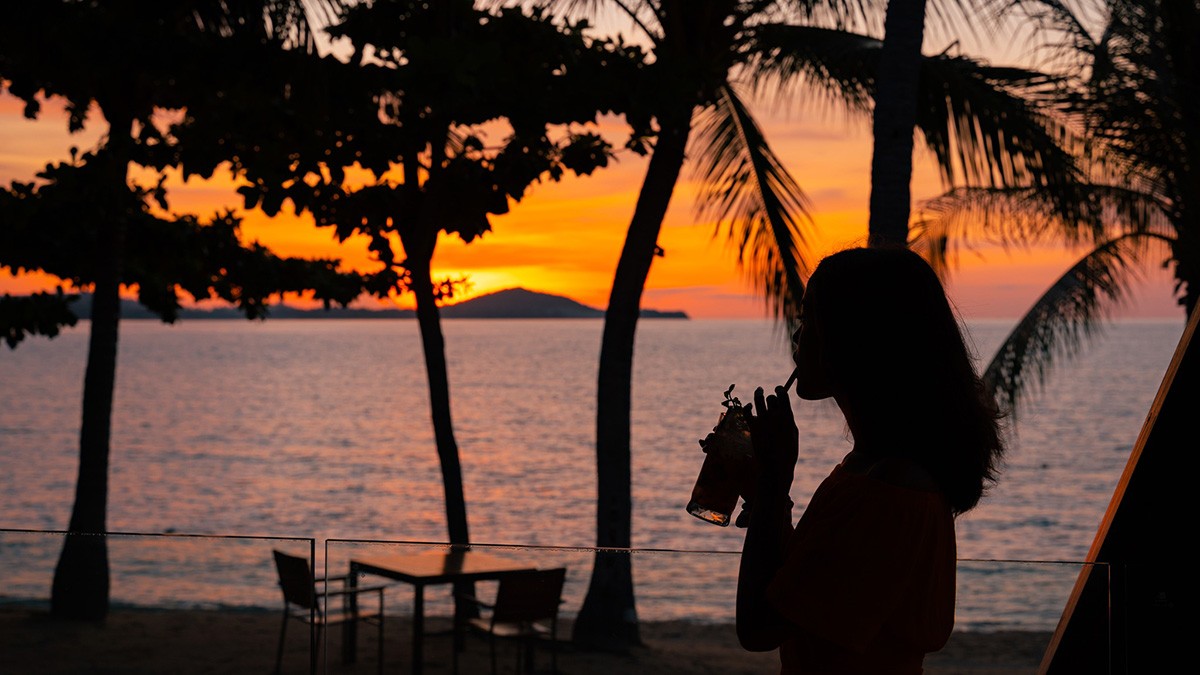 Scenic view of Koh Samui coastline at sunset, with a traveler on a scooter enjoying the breathtaking landscape