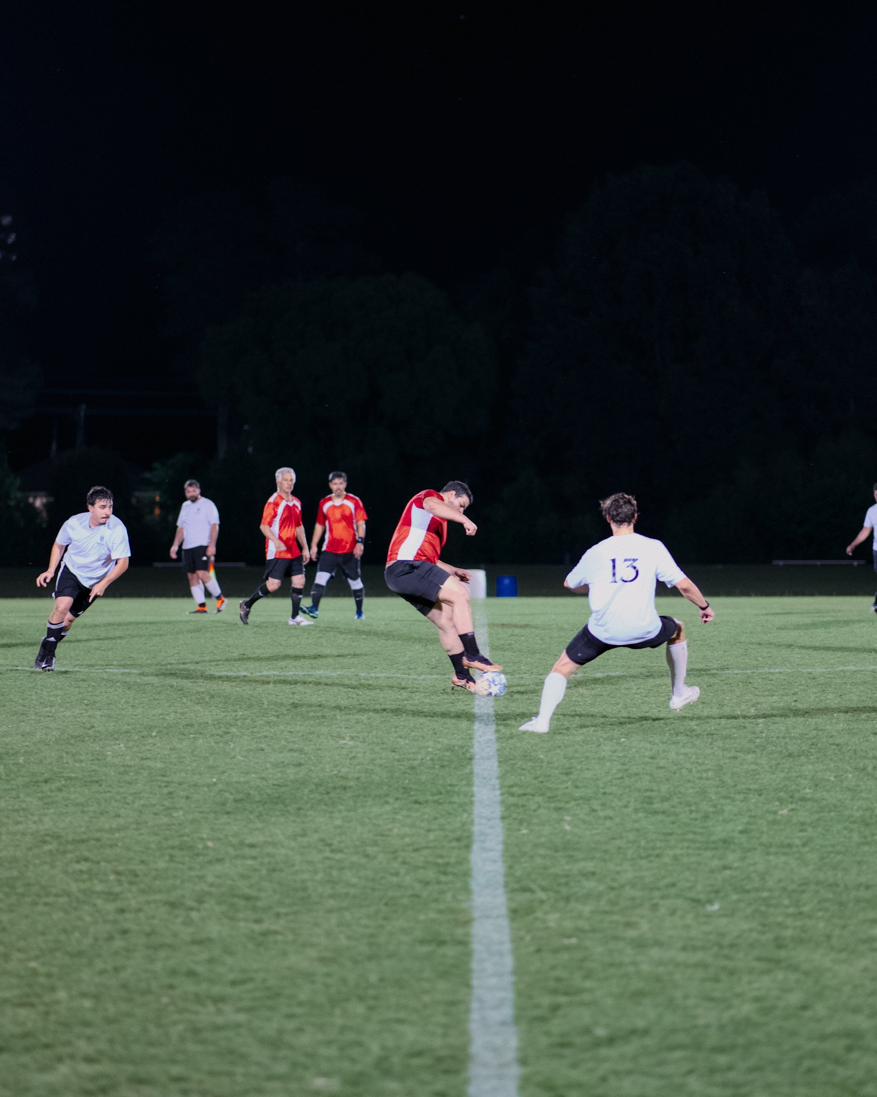 AlFursan FC player in red takes a shot as a defender in white closes in