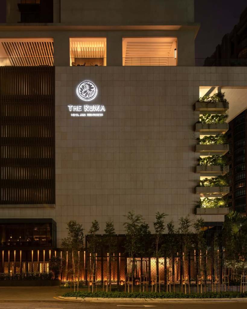 Night view of The Ruma Hotel and Residences exterior, featuring illuminated signage and decorative greenery.