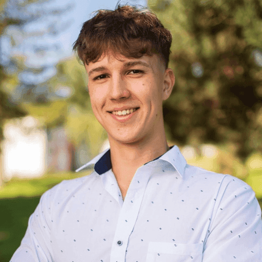 A woman with tousled brown hair wears round orange sunglasses and a floral-patterned blouse. Her expression is neutral, conveying a vintage vibe.