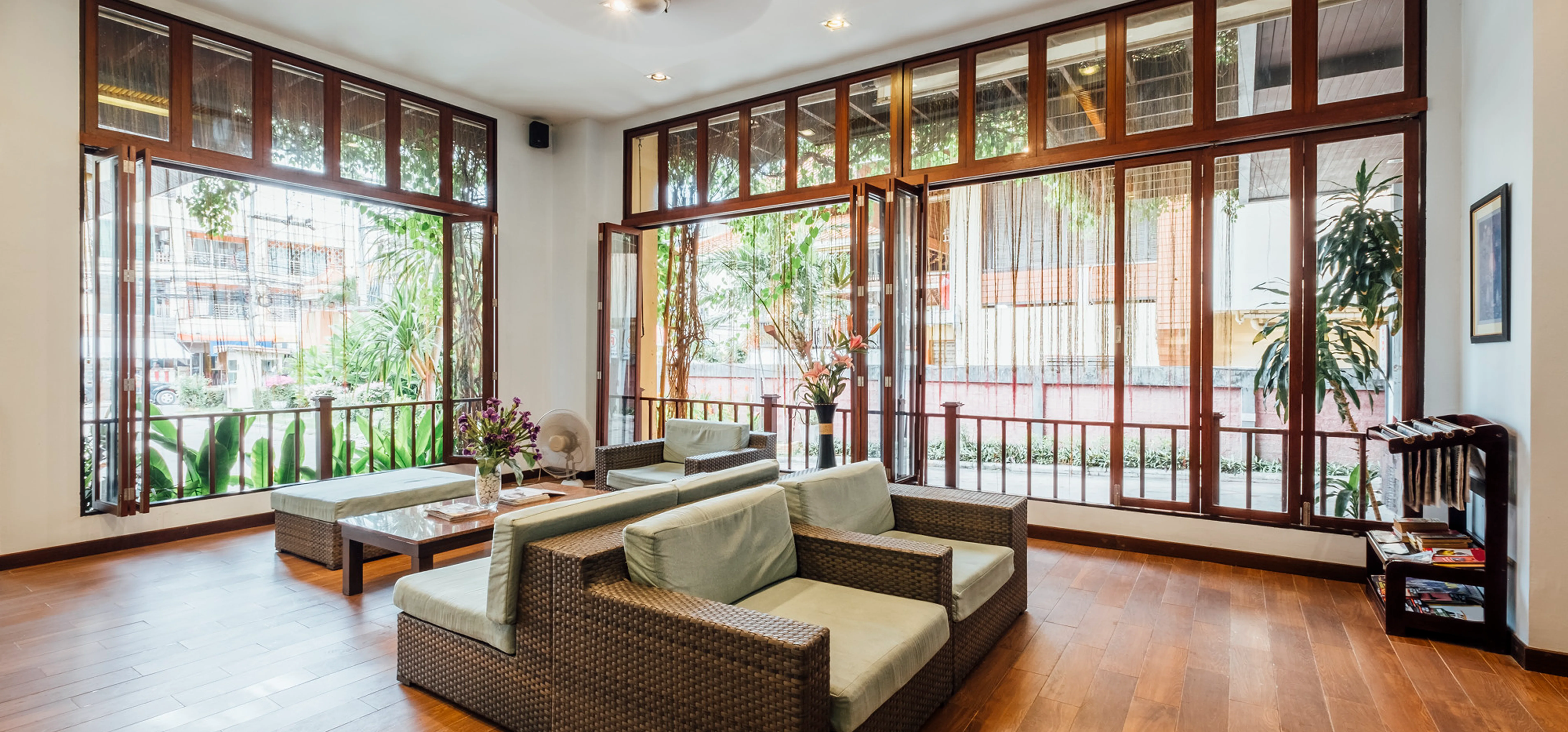 Bright interior lounge with wicker furniture and large wood-framed glass doors overlooking a tropical patio.