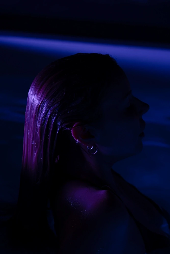 Guest resting upright in a cold-plunge pool, illuminated with deep purple and blue tones.