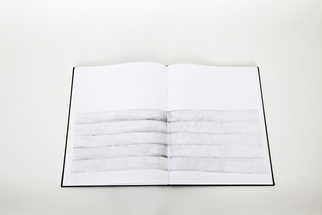 An open book lies flat on a white surface. The pages are blank except for a horizontal drawing composed of multiple horizontal gray lines. The lines are evenly spaced and run parallel to each other. The book has a black cover, and the pages are white. The drawing is centered on the open pages.