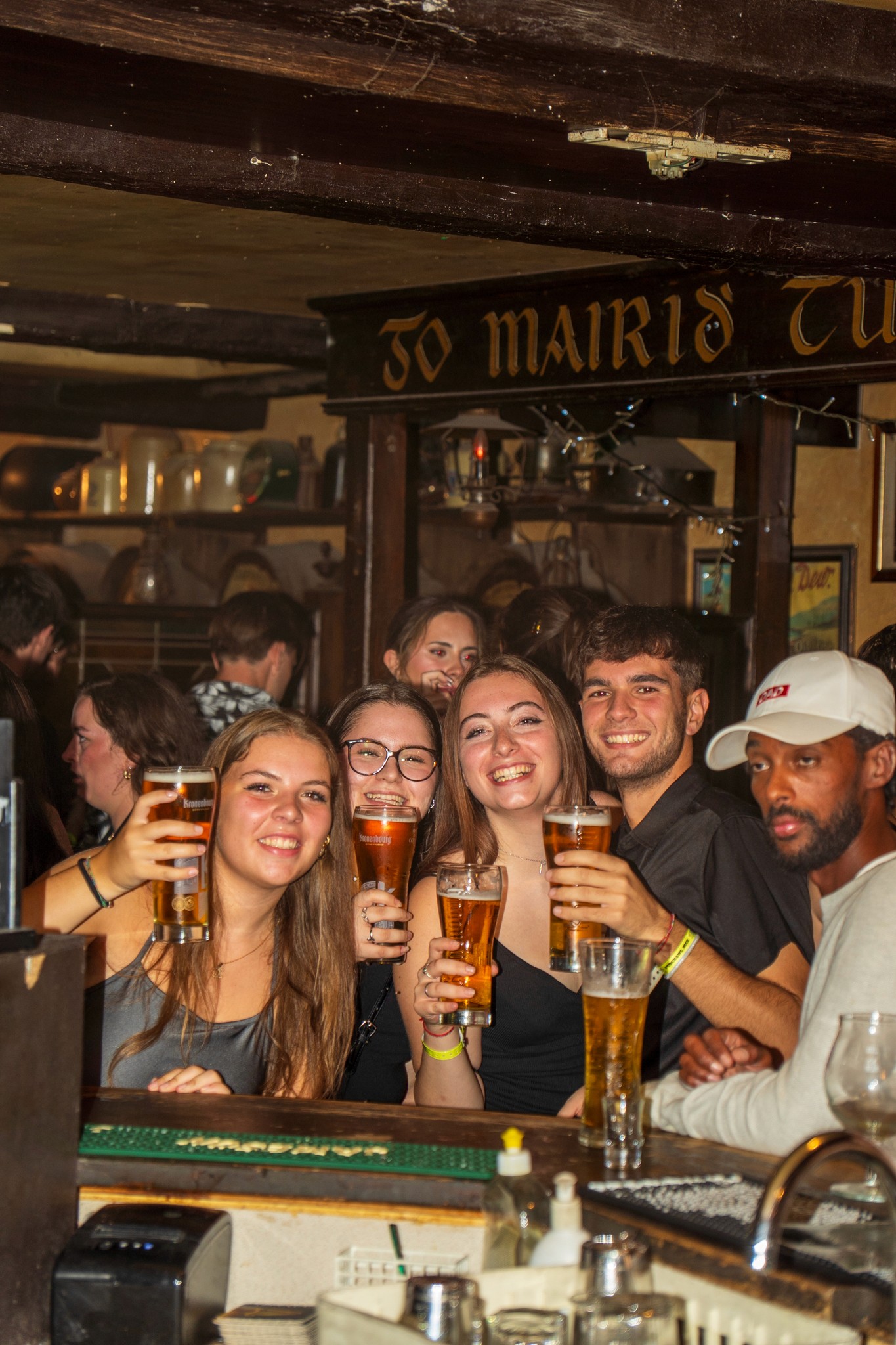 A lively bar scene in Nice with travelers laughing together, drinks in hand, and warm lights reflecting off the walls late at night.