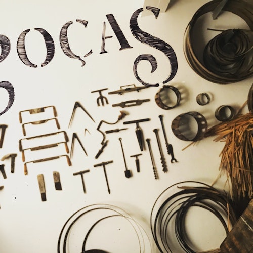 Diversas ferramentas de metal e objetos circulares dispostos em uma superfície branca, com o texto parcialmente visível "POÇAS" acima deles.