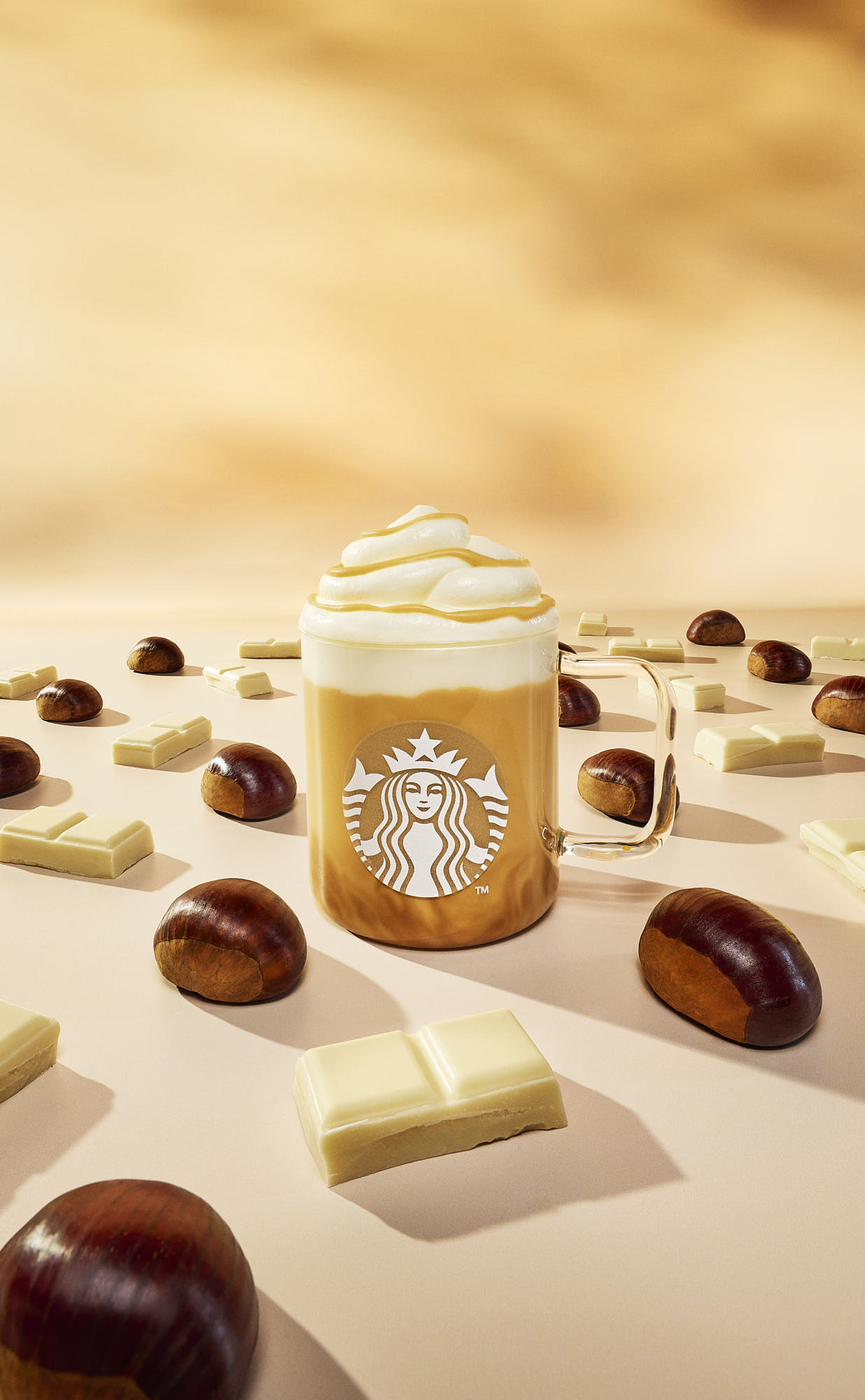 A coffee latte of creamy top surrounded by scattered chocolate cubes and chestnuts on a light background.