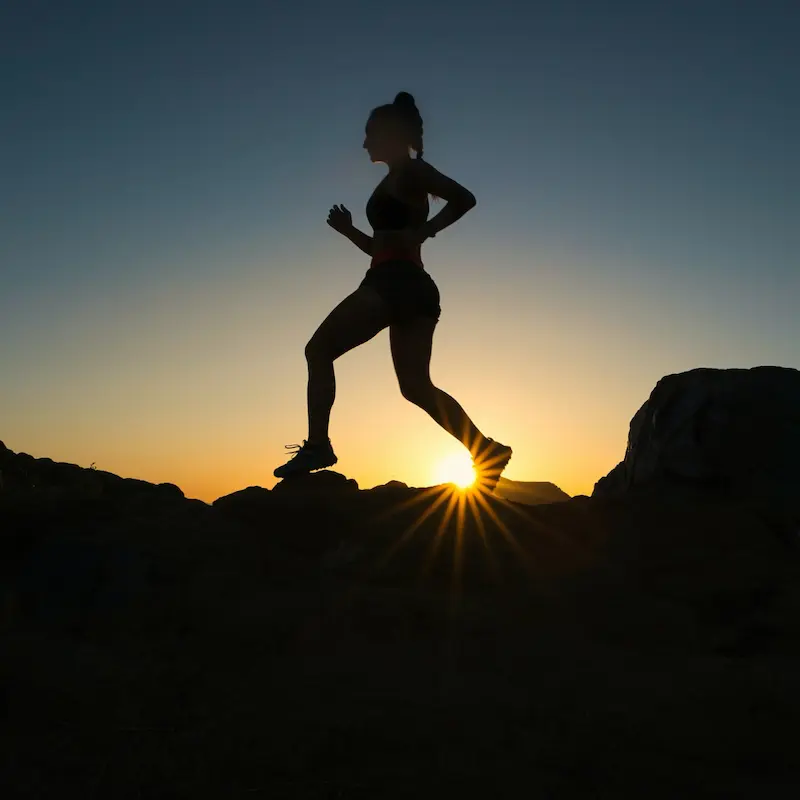 Une femme court sur un terrain rocailleux au levé du soleil