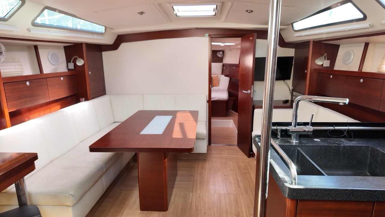 Hanse 470e sailing yacht main saloon featuring EcoDeck light oak composite cabin flooring, U-shaped white leather dinette seating with mahogany dining table, open forward cabin door, granite galley sink, and hull portlights