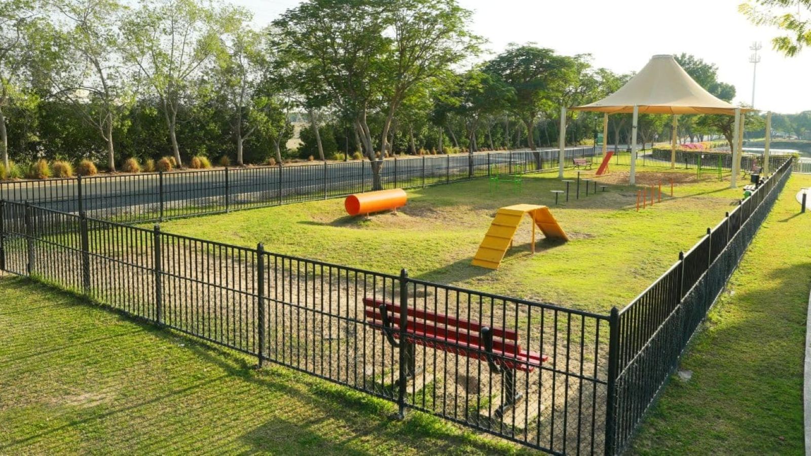 The Springs 8 Dog Park with black fencing, tunnels, ramps, benches, and a shaded area.