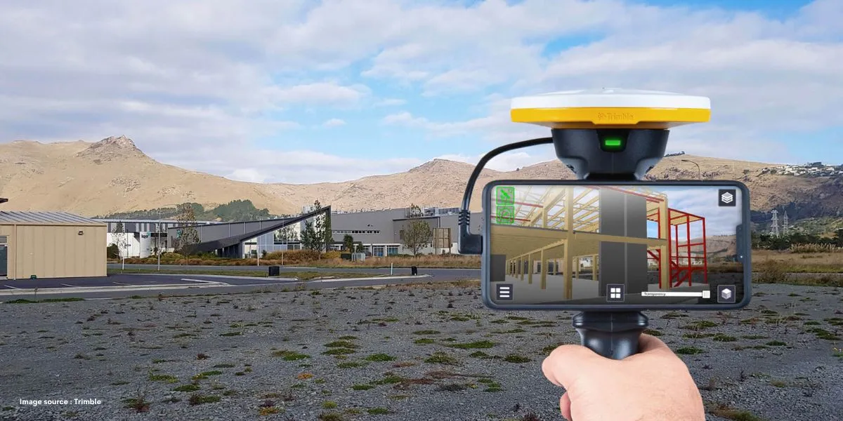 A man stands while two people sit at a table in an office setting, smiling and engaged in conversation. The mood is friendly and collaborative.