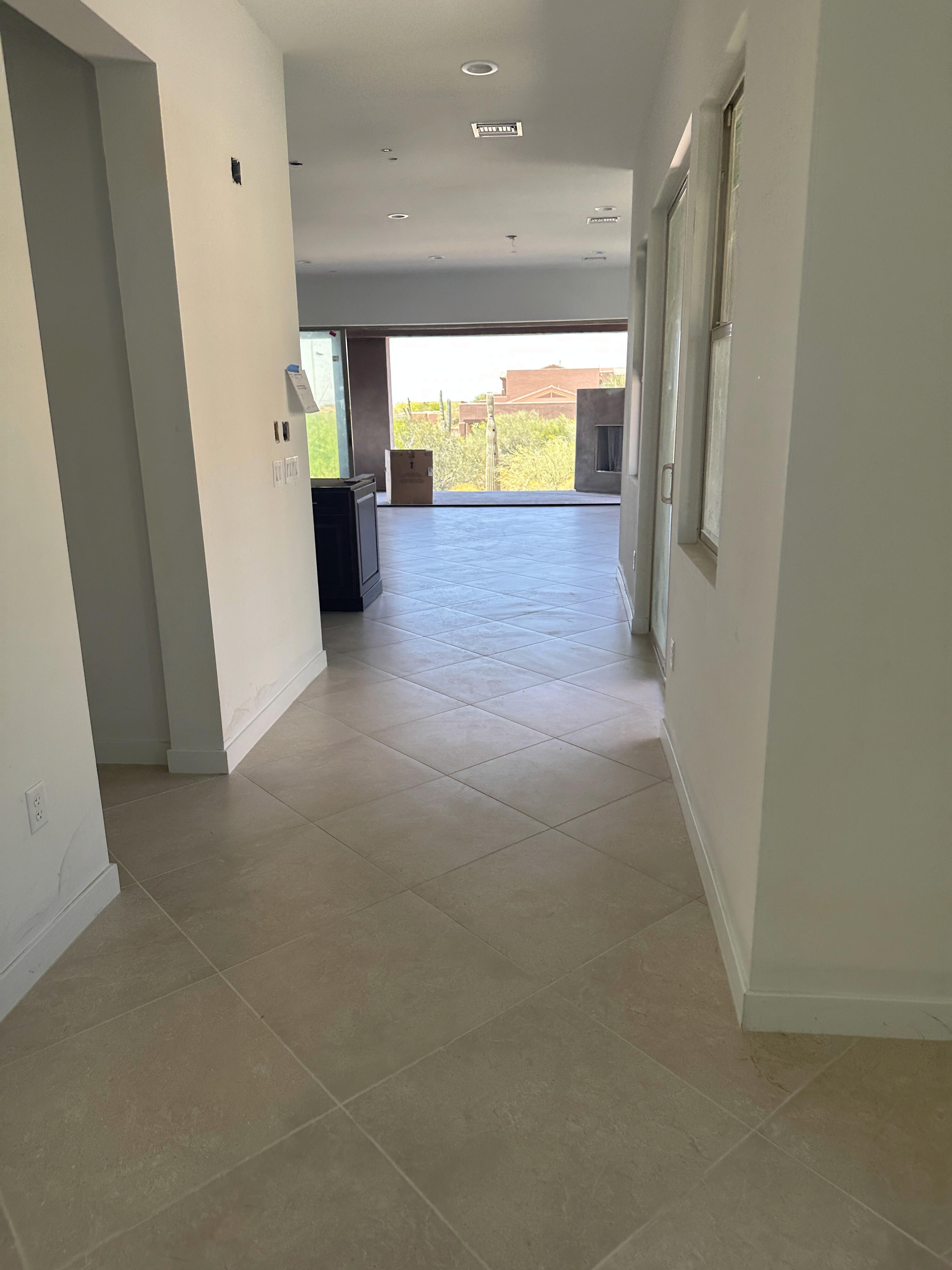 Modern hallway with beige tile flooring, leading to an open living area with large windows and a desert view during construction.