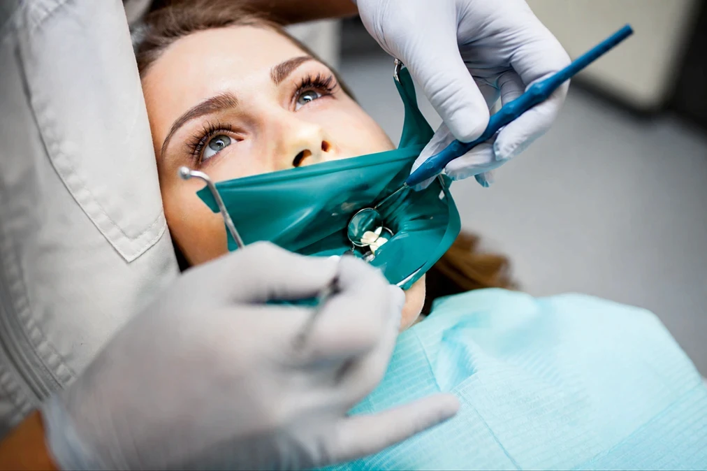 Professional dentist using a dental light and mirror during a routine oral hygiene examination.