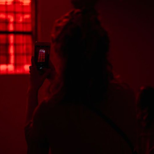 Seorang siluet dalam cahaya merah mengambil foto dengan ponselnya, menangkap jendela yang dilatarbelakangi cahaya merah.