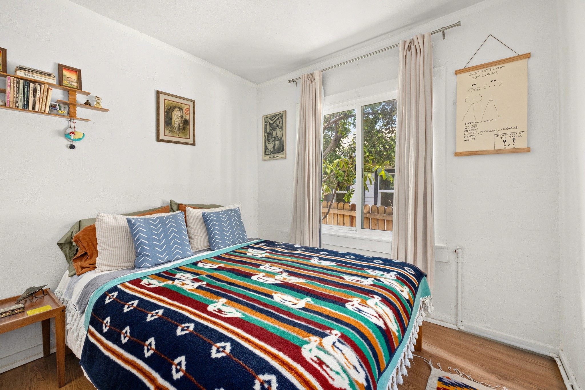 Bright, cozy bedroom at 3456 plata, with a patterned quilt, two windows, and decorative wall art. Wood flooring adds warmth.