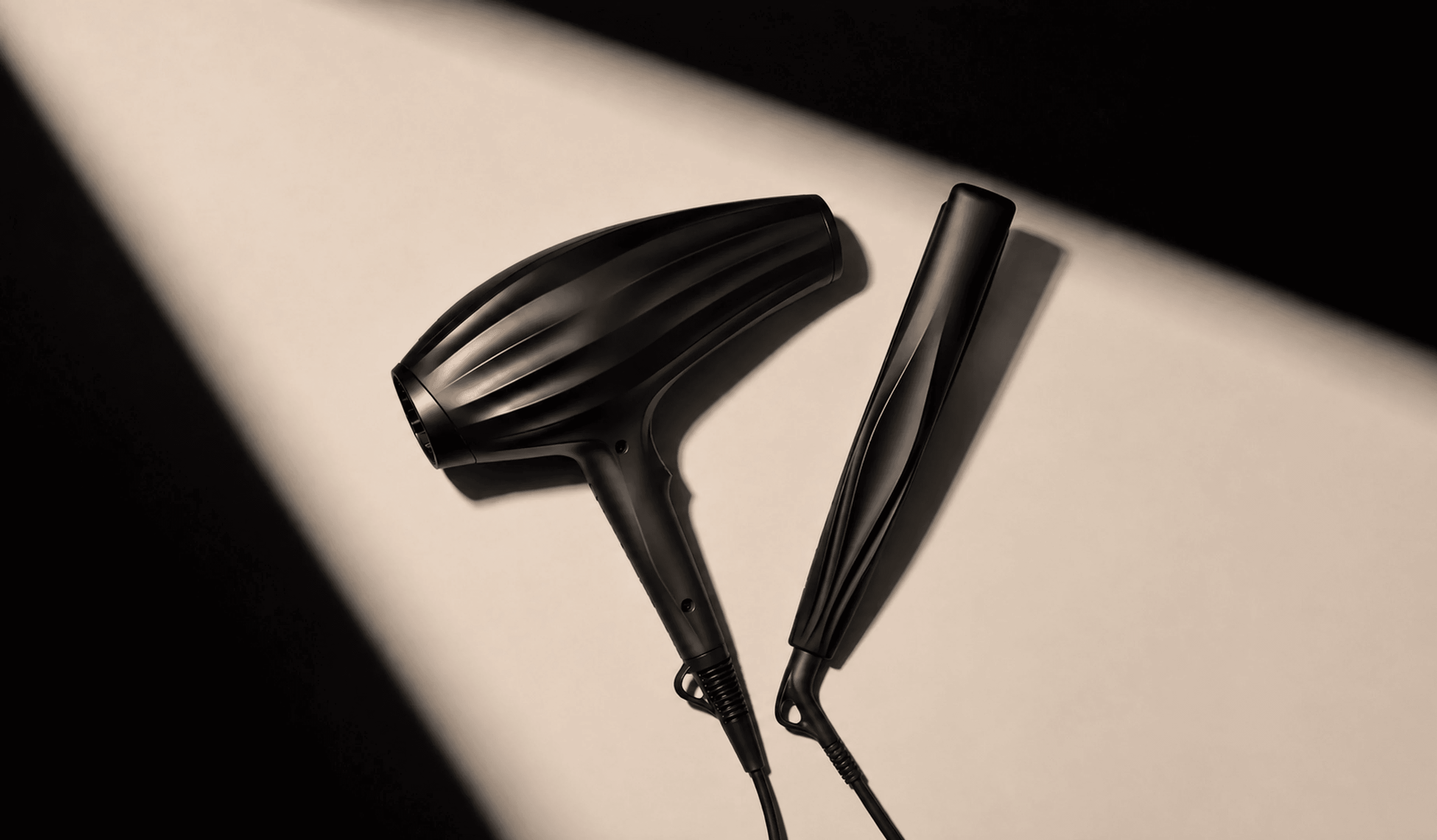 The Neuro dryer and straightener side by side on a beige surface, cut by a hard diagonal shadow.