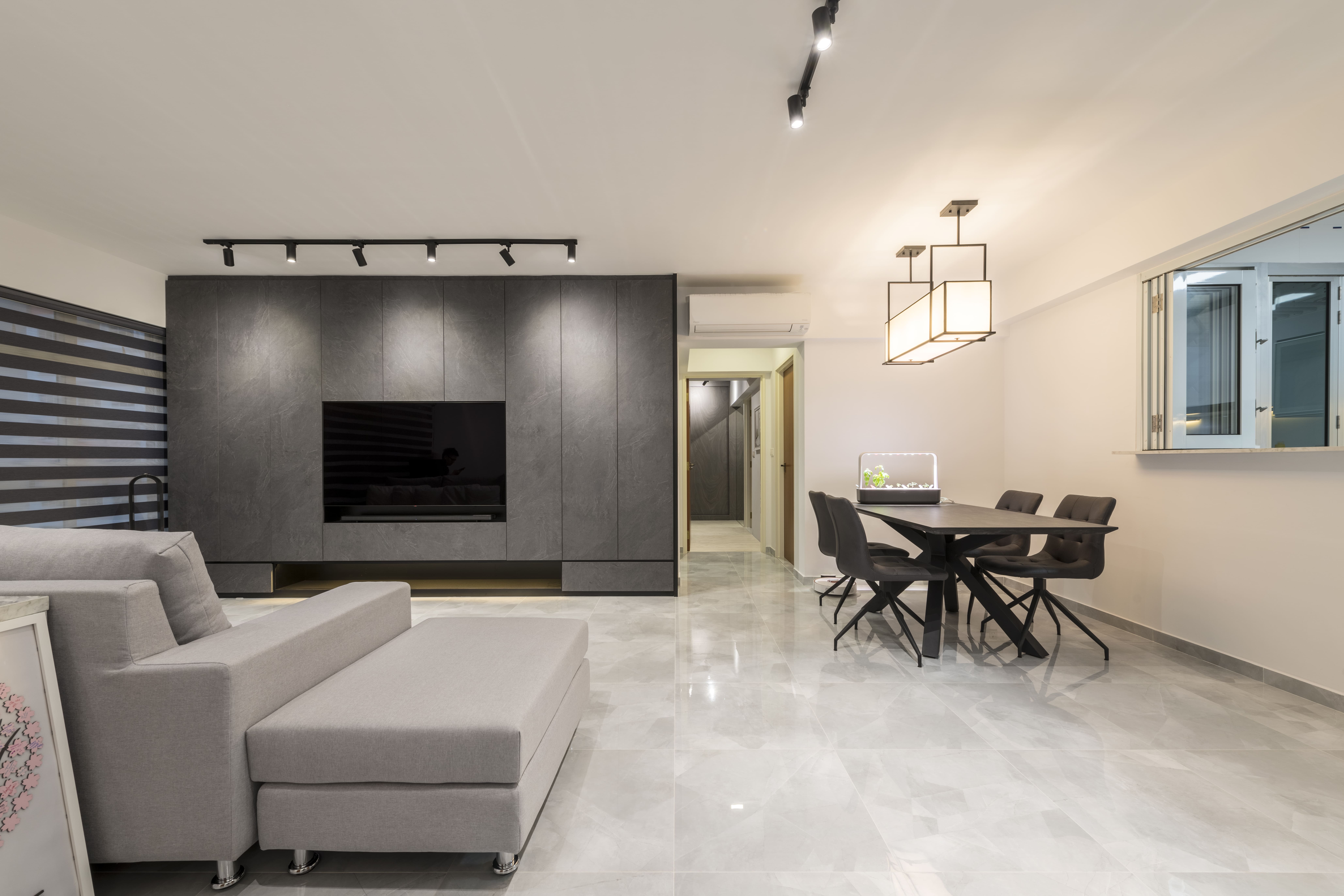A sleek, modern living room with a grey sectional sofa, marble-look flooring, and a feature wall with a flush-mounted TV, creating a seamless minimalist aesthetic.