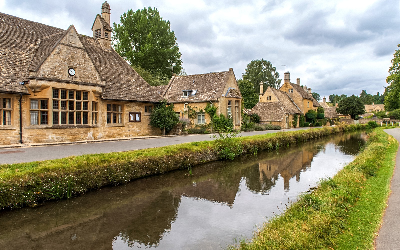 Cotswolds village street with stone cottages and canal, part of a guided day tour from London.
