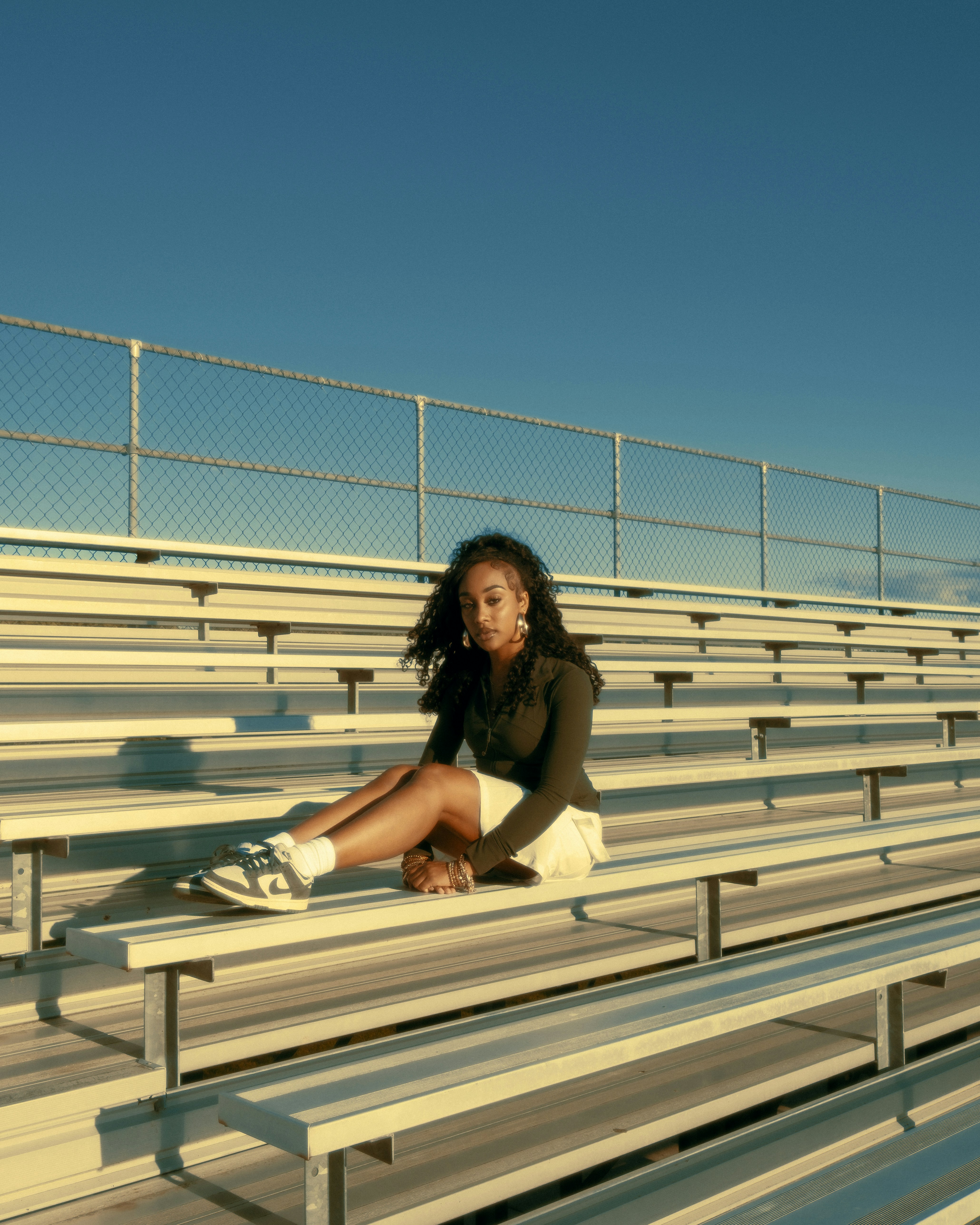 Young woman sitting on bleachers under a clear blue sky