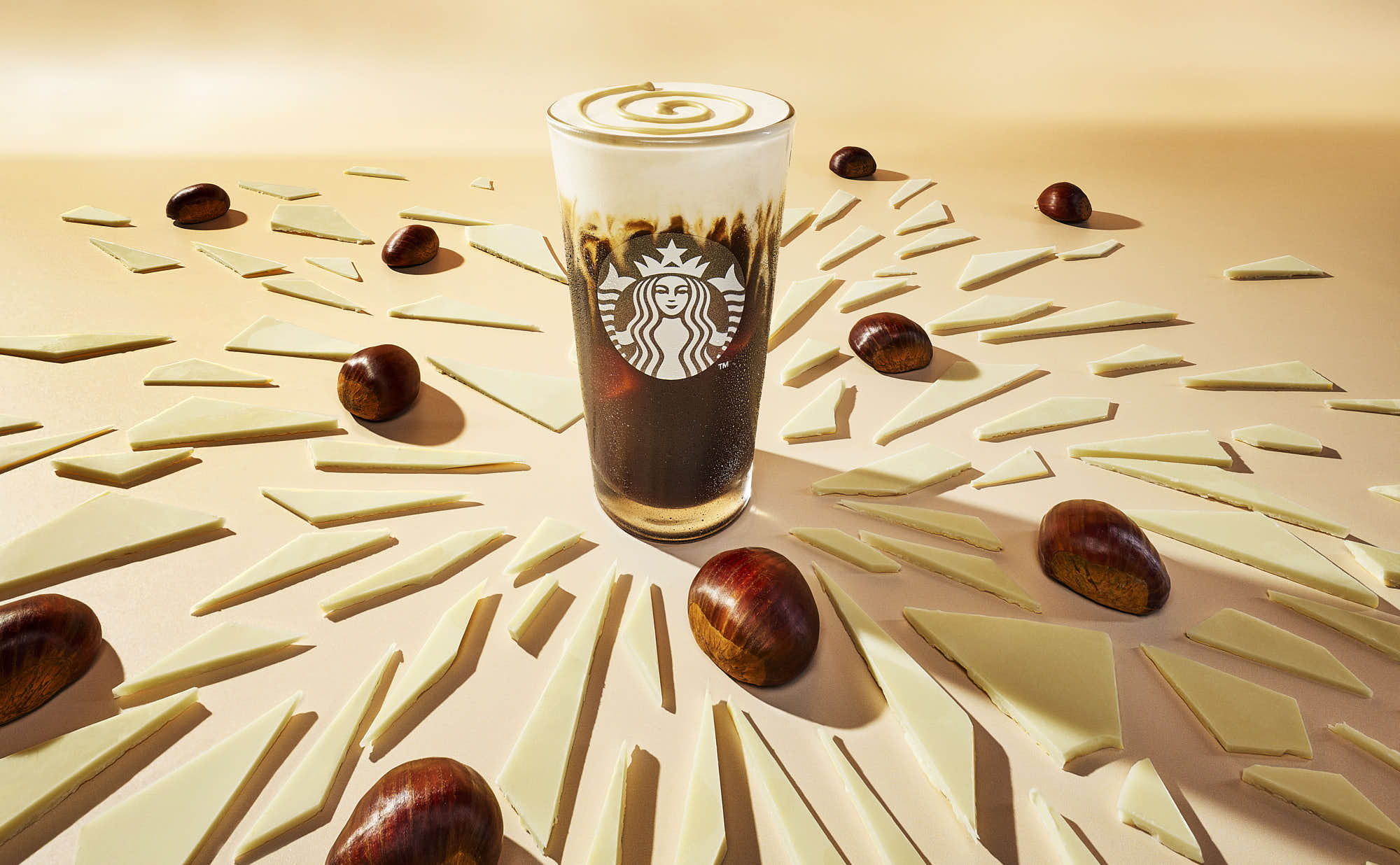 A glass of iced coffee surrounded by chocolate shards, set against a warm, sandy background.