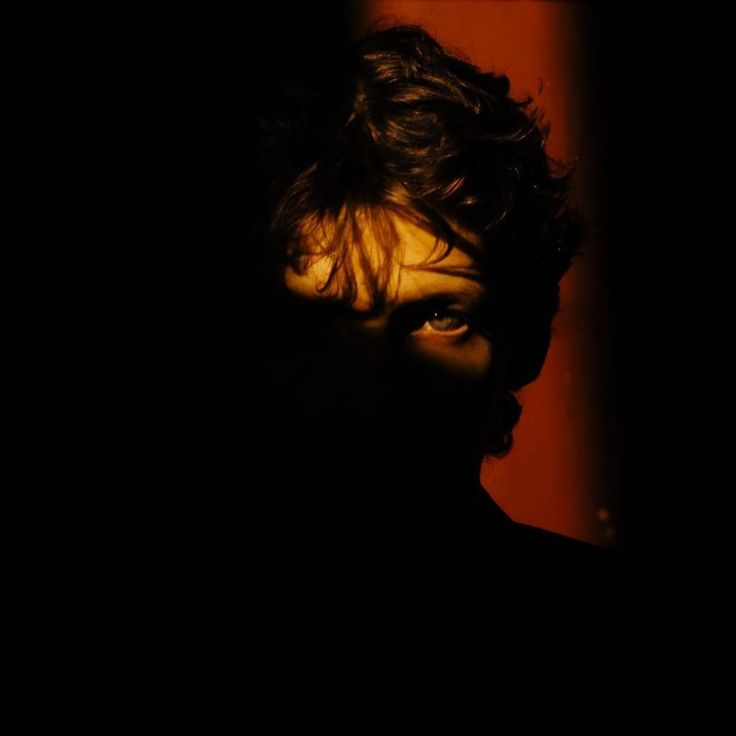 Young woman with curly hair wearing a white shirt and pants sitting on a couch in warm, dim lighting.