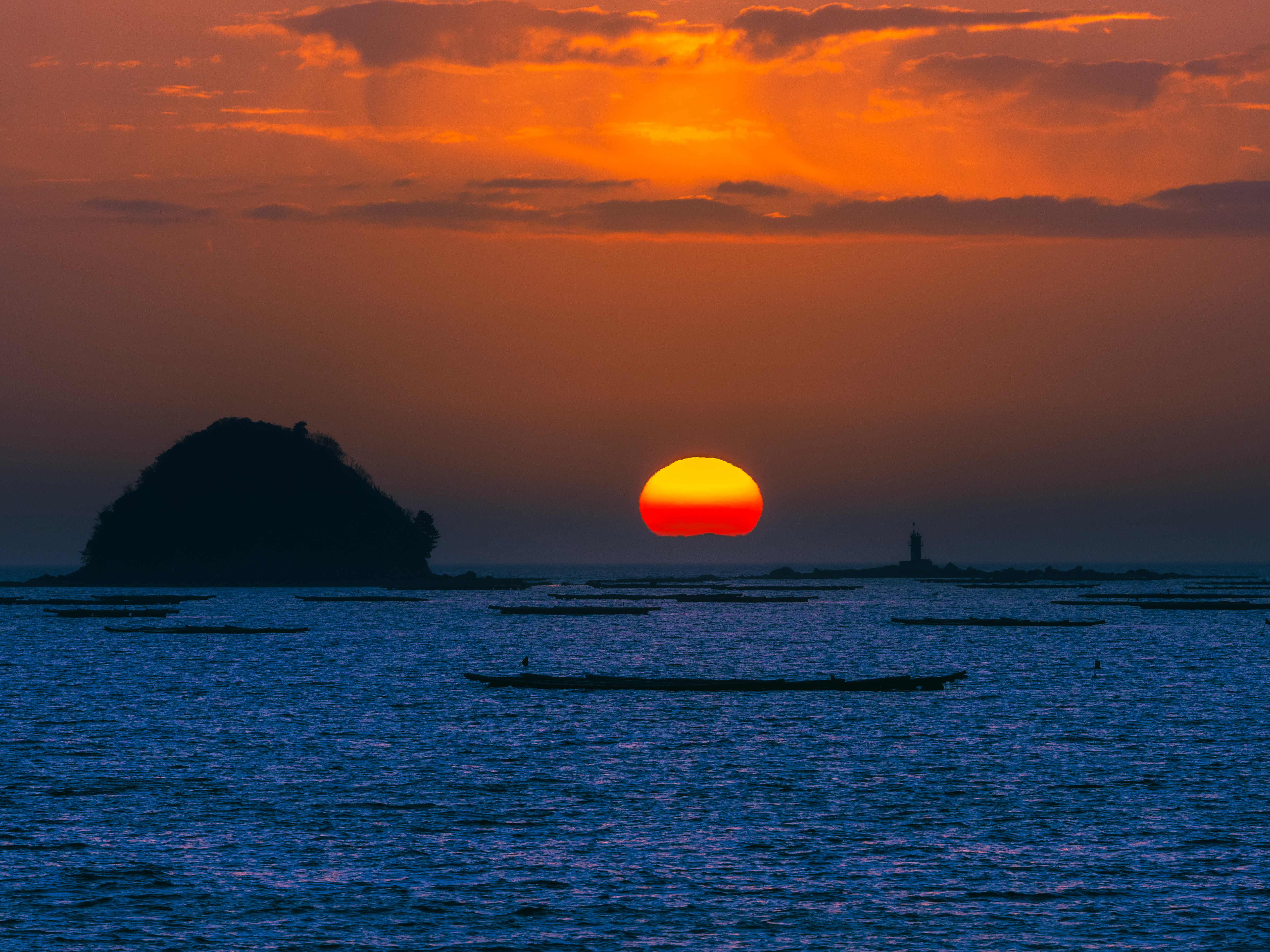 Bright orange sunset against dark blue waters and a hazy sky