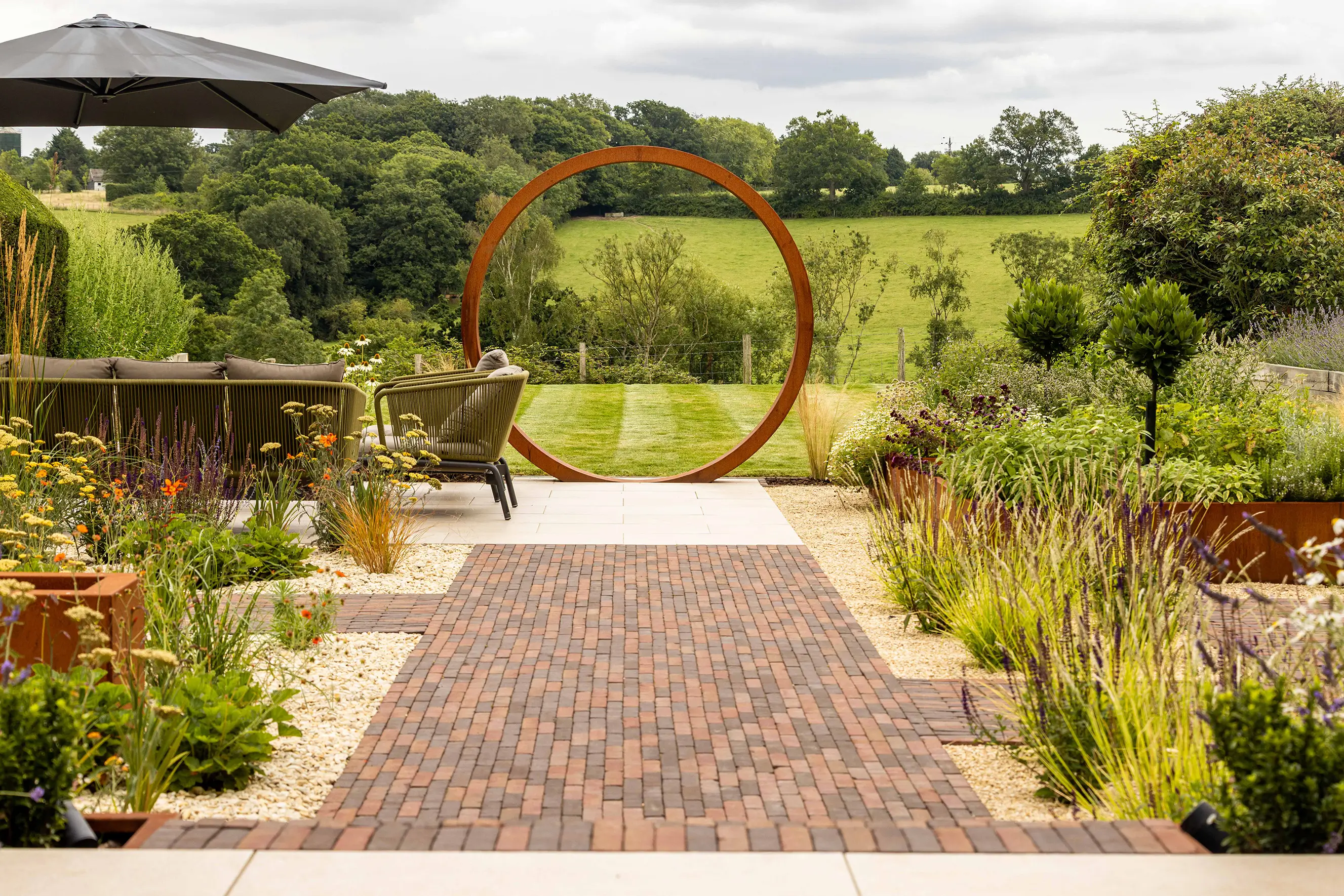 A serene garden path leads through lush greenery, framed by vibrant flowers and a distant gazebo.