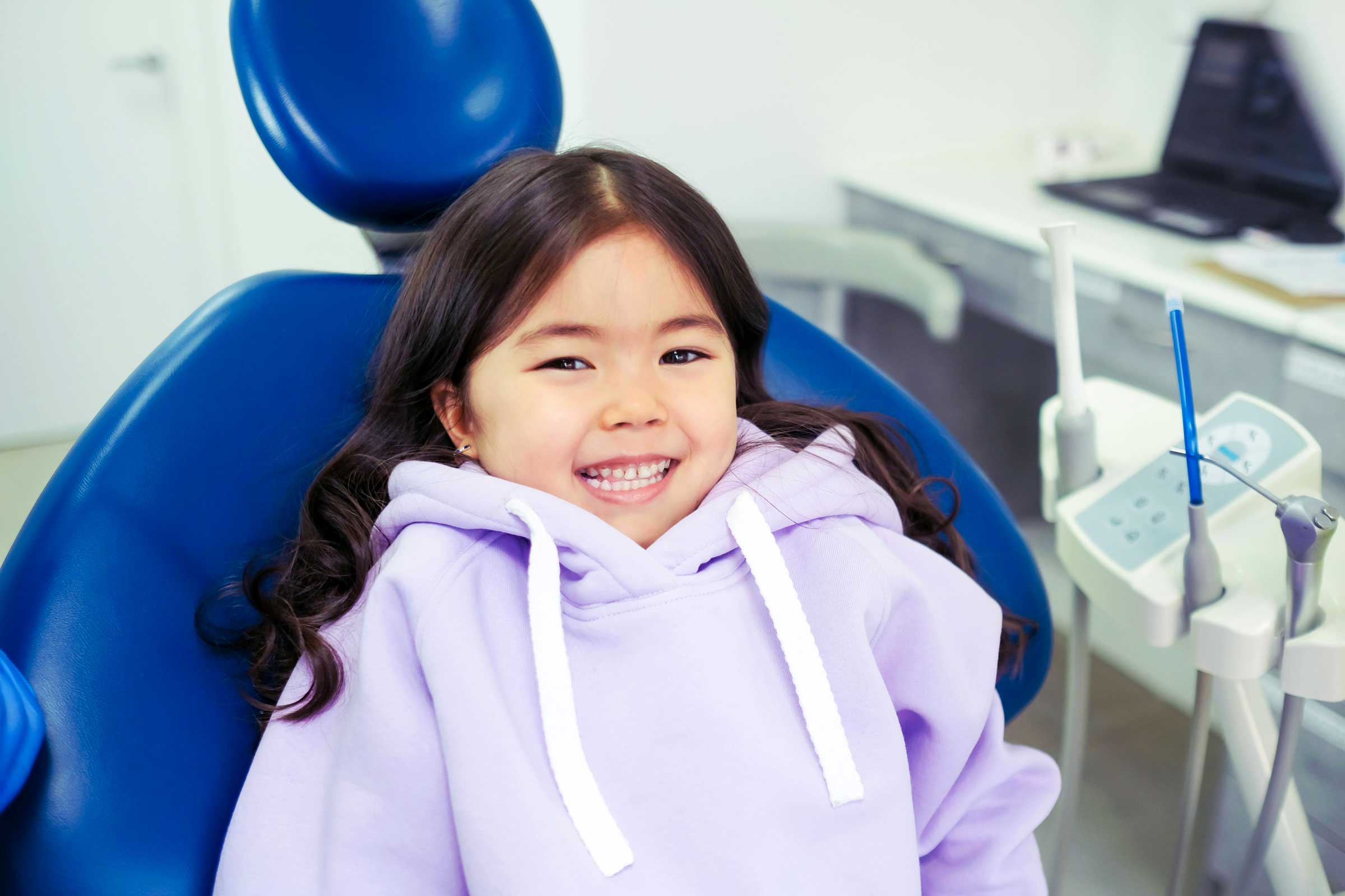 A cute child sitted in the patient chair at a Dentist Room, smilling to the camera.