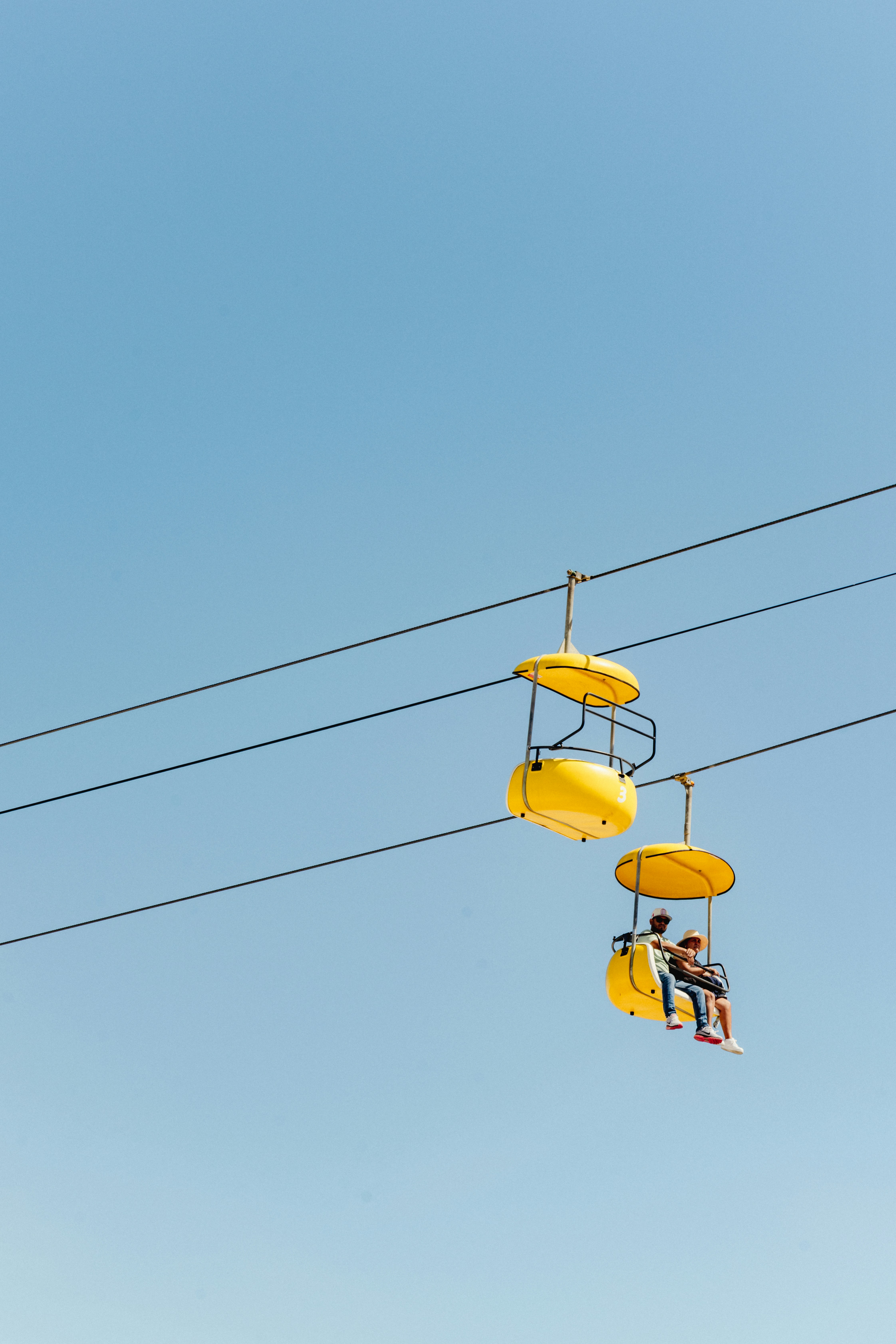 Two yellow gondolas ascend against a clear blue sky.