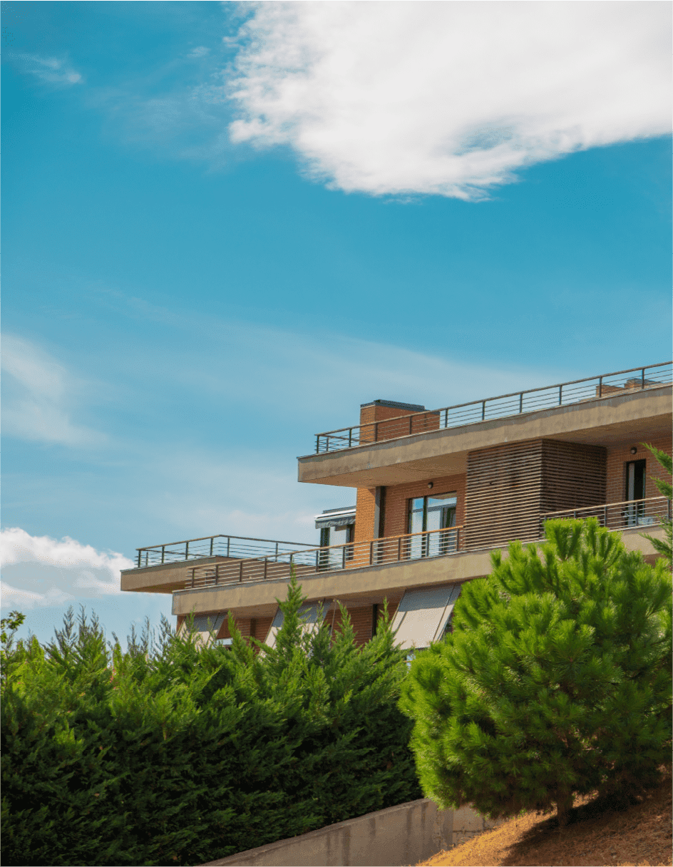 Modern building against a clear blue sky, surrounded by lush greenery and distant clouds.
