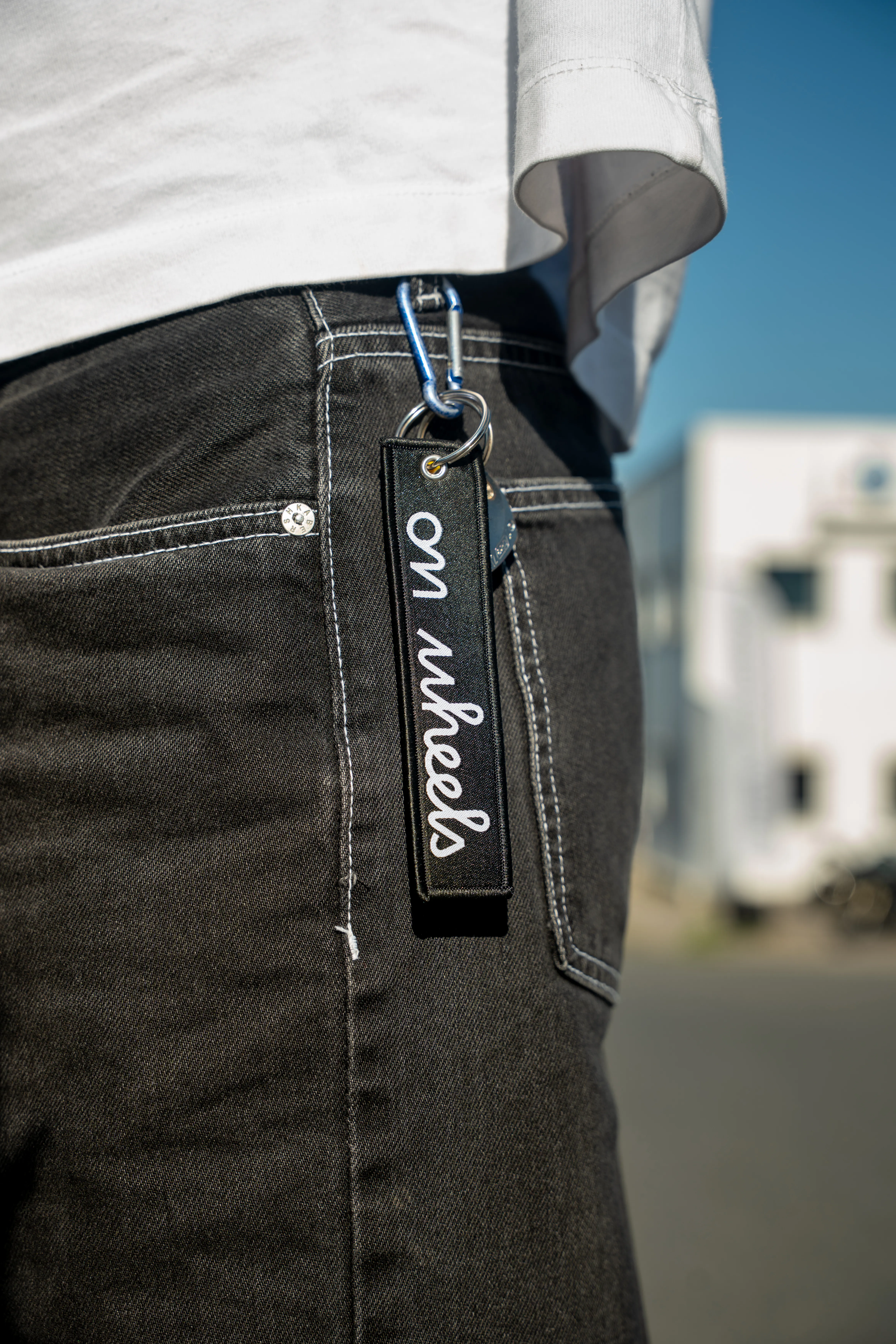 Porte-clés On Wheels tenu à la main avec slogan organiser échanger rouler, fond ciel bleu