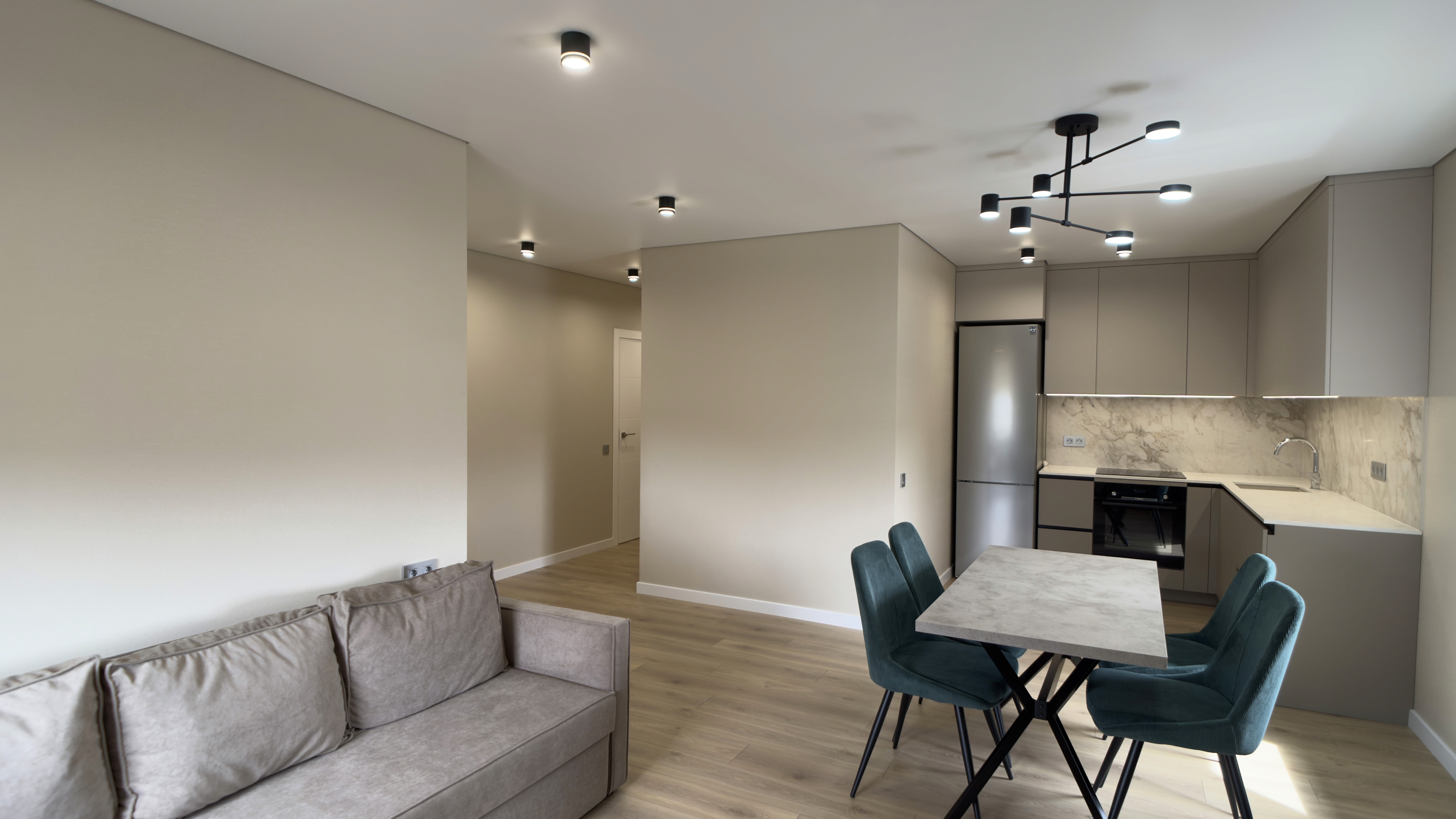 Вітальня з диваном, кухнею у глибині кімнати та яскравим освітленням