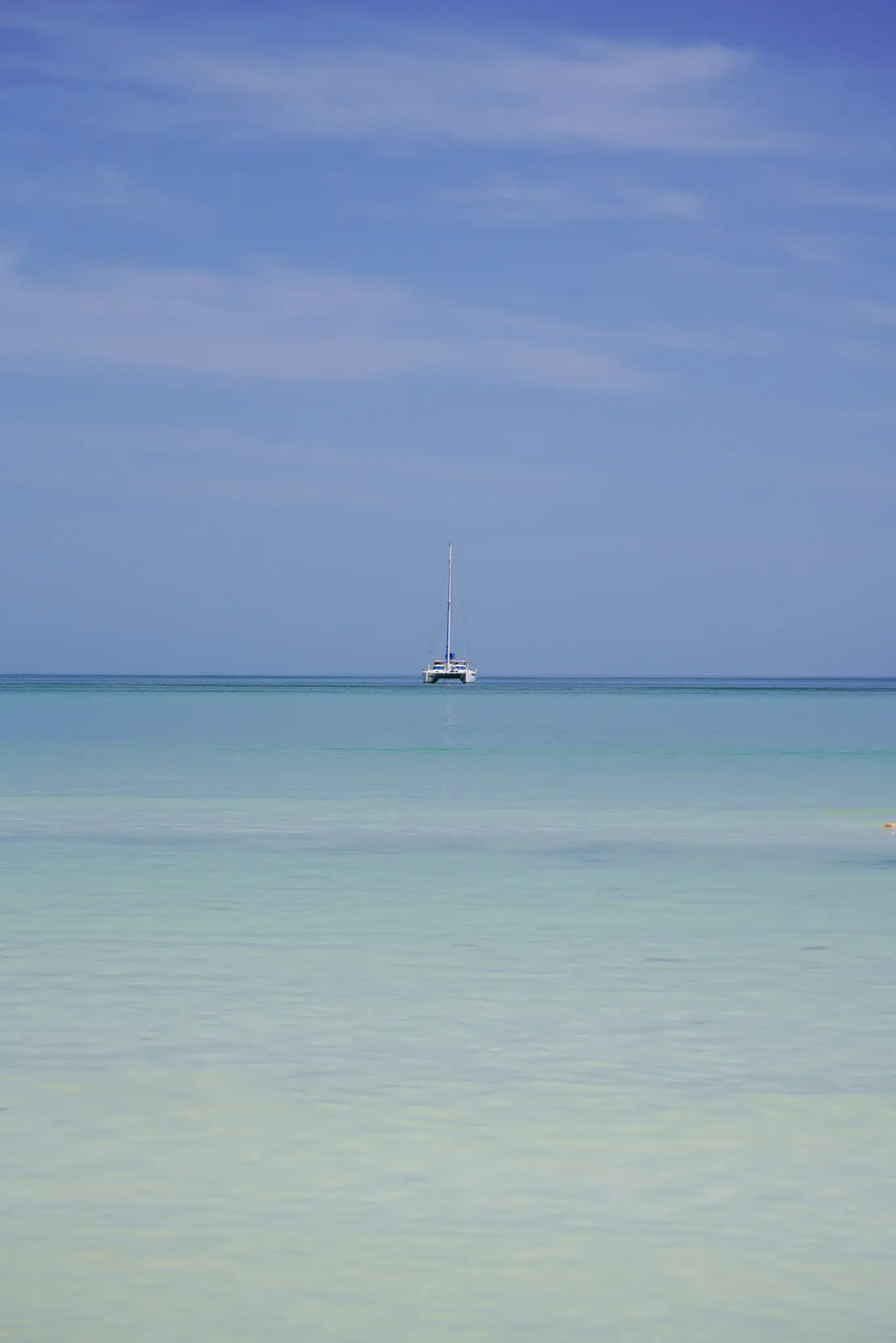 Catamaran isolé à l’horizon sur une mer calme aux eaux turquoise, au large d’Holbox