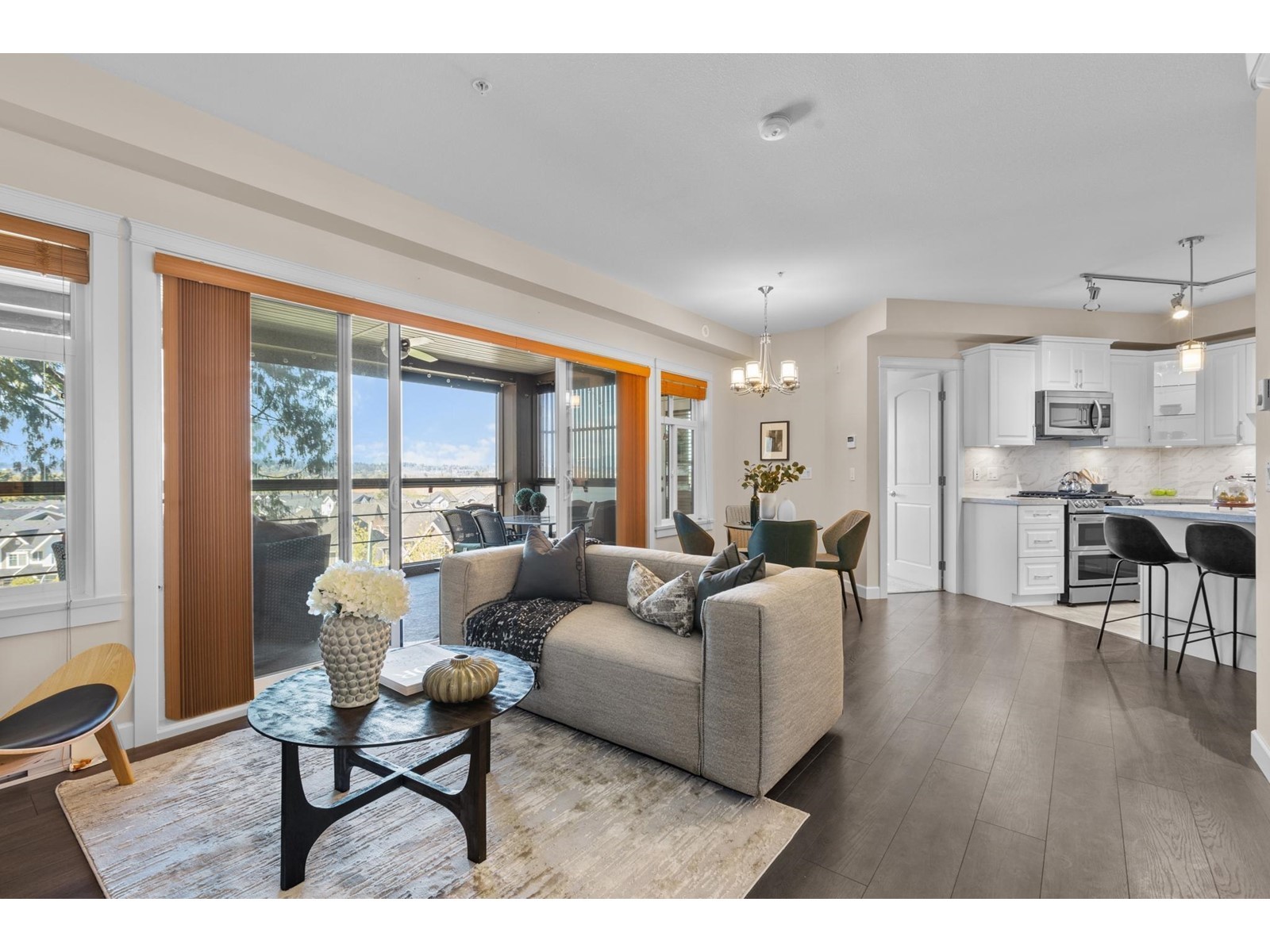 Modern living room featuring a couch, coffee table, and large windows with an adjacent kitchen visible.